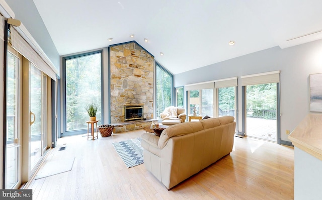 living room featuring high vaulted ceiling, a fireplace, and light hardwood / wood-style floors