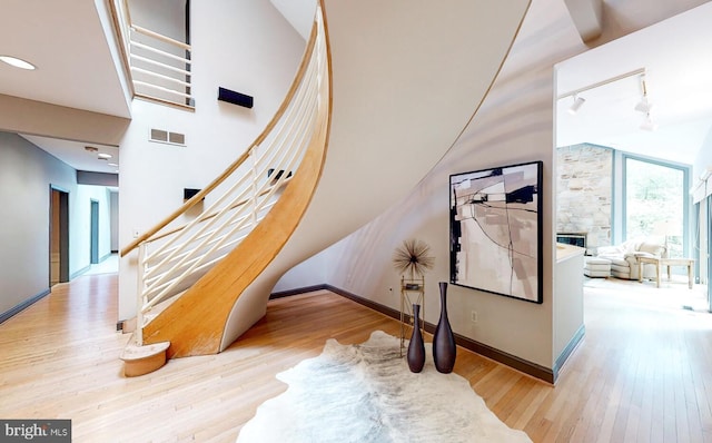 stairway with a high ceiling, wood-type flooring, a stone fireplace, and track lighting