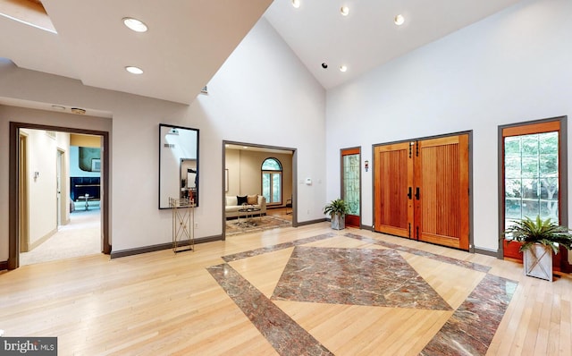 entryway featuring light wood finished floors, recessed lighting, high vaulted ceiling, and baseboards