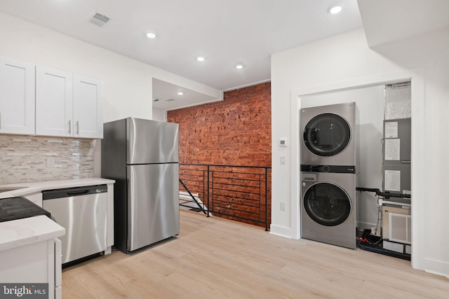 kitchen featuring light hardwood / wood-style flooring, white cabinetry, stacked washing maching and dryer, backsplash, and stainless steel appliances