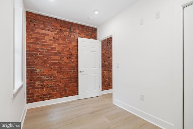 spare room with light hardwood / wood-style floors and brick wall