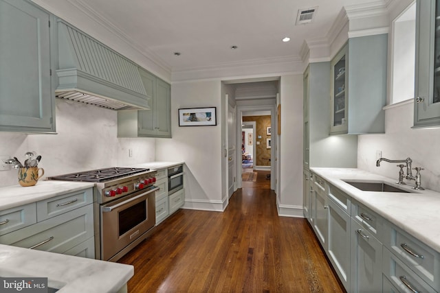 kitchen with custom exhaust hood, light countertops, appliances with stainless steel finishes, glass insert cabinets, and a sink