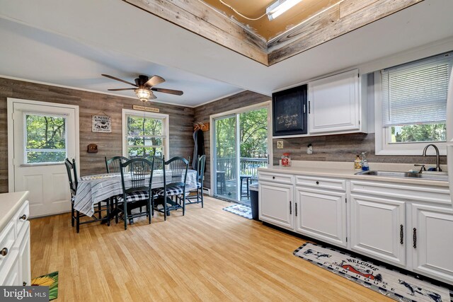 kitchen featuring light hardwood / wood-style flooring, white cabinets, sink, and wooden walls