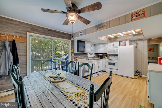 dining area with ceiling fan, sink, light hardwood / wood-style floors, and wood walls