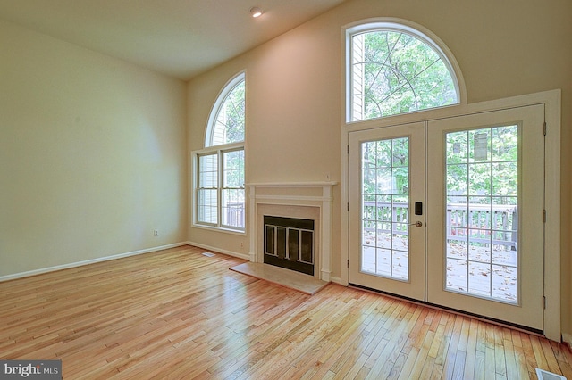 unfurnished living room featuring a healthy amount of sunlight, light hardwood / wood-style flooring, and french doors