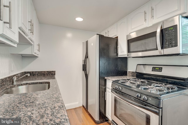 kitchen featuring white cabinets, appliances with stainless steel finishes, dark stone countertops, light wood-type flooring, and a sink