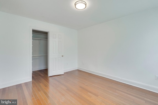 unfurnished bedroom featuring light wood-style floors, a closet, a spacious closet, and baseboards