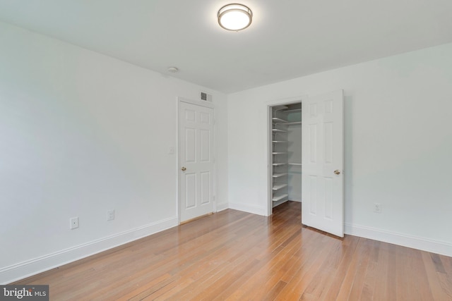 unfurnished bedroom featuring wood finished floors, visible vents, baseboards, a spacious closet, and a closet