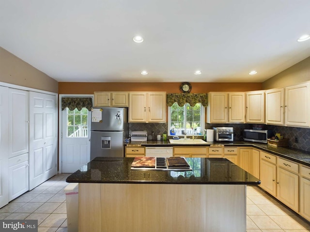 kitchen featuring light brown cabinetry, dark stone countertops, stainless steel appliances, backsplash, and light tile patterned floors