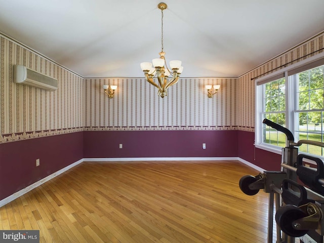 exercise area with an inviting chandelier, lofted ceiling, a wall unit AC, and hardwood / wood-style flooring