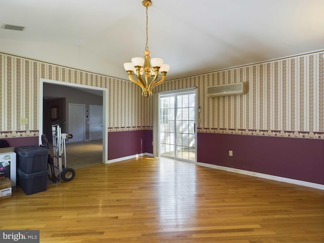 spare room with vaulted ceiling, a wall mounted air conditioner, hardwood / wood-style floors, and an inviting chandelier