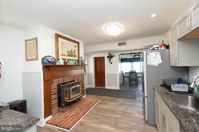 kitchen with a wood stove, light hardwood / wood-style floors, white cabinetry, sink, and stainless steel fridge