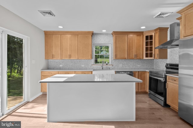 kitchen featuring visible vents, a kitchen island, stainless steel appliances, wall chimney range hood, and a sink