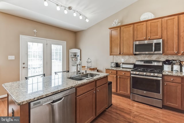 kitchen featuring light wood-type flooring, rail lighting, appliances with stainless steel finishes, a kitchen island with sink, and vaulted ceiling