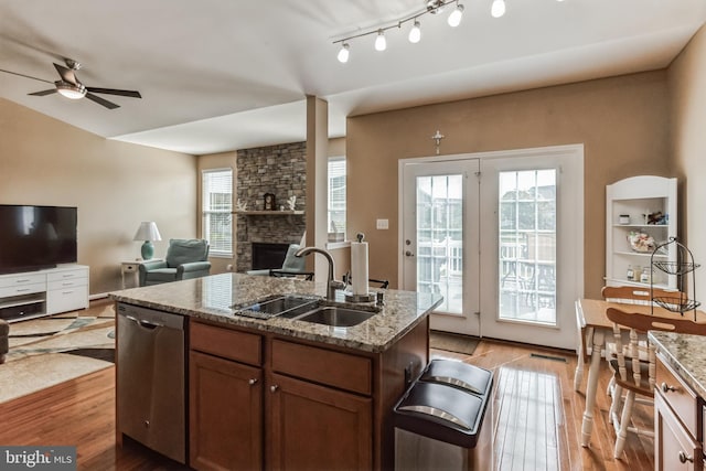 kitchen with sink, light stone counters, light hardwood / wood-style floors, a stone fireplace, and stainless steel dishwasher