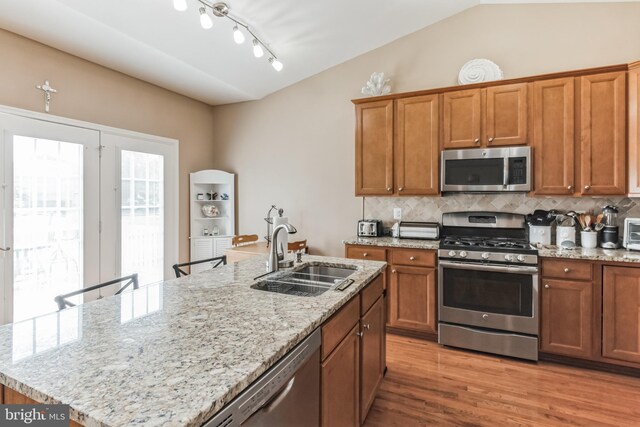 kitchen featuring rail lighting, a center island with sink, stainless steel appliances, and vaulted ceiling