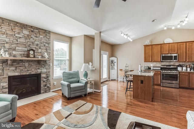 kitchen with sink, appliances with stainless steel finishes, a kitchen breakfast bar, light stone countertops, and a center island with sink