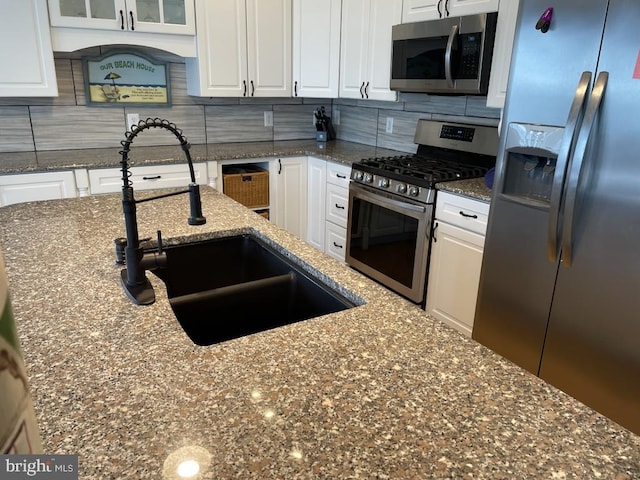 kitchen with white cabinetry, appliances with stainless steel finishes, stone countertops, backsplash, and sink