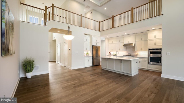 kitchen featuring an island with sink, hanging light fixtures, stainless steel appliances, light countertops, and under cabinet range hood