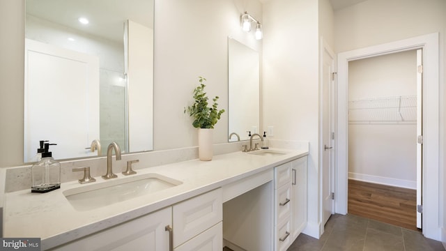 bathroom featuring a walk in closet, tile patterned flooring, a sink, and double vanity