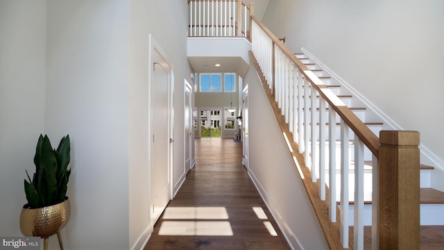 hallway featuring a towering ceiling, stairs, baseboards, and wood finished floors