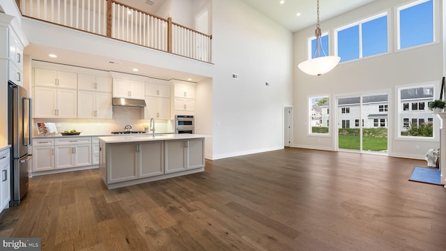 kitchen with open floor plan, hanging light fixtures, appliances with stainless steel finishes, light countertops, and an island with sink