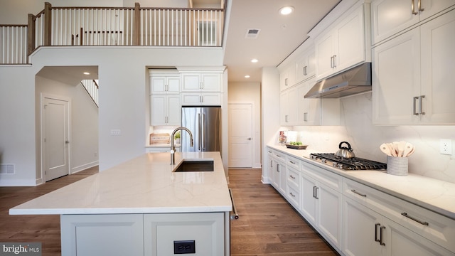 kitchen with a kitchen island with sink, under cabinet range hood, white cabinets, appliances with stainless steel finishes, and light stone countertops