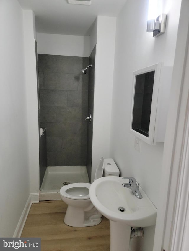 bathroom with wood-type flooring, sink, toilet, and tiled shower