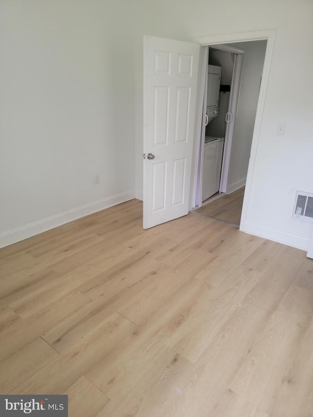 unfurnished room with stacked washer and dryer and light hardwood / wood-style flooring