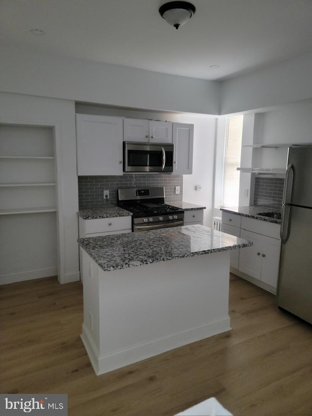 kitchen featuring a center island, appliances with stainless steel finishes, white cabinets, light hardwood / wood-style flooring, and light stone counters