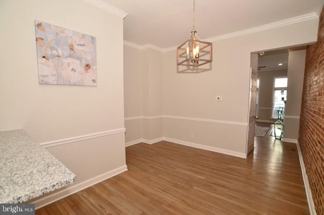 unfurnished dining area featuring ornamental molding, brick wall, dark wood-type flooring, and a chandelier