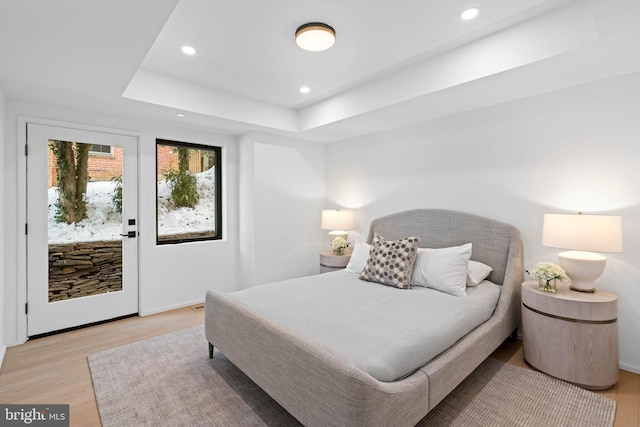 bedroom with light hardwood / wood-style floors and a tray ceiling