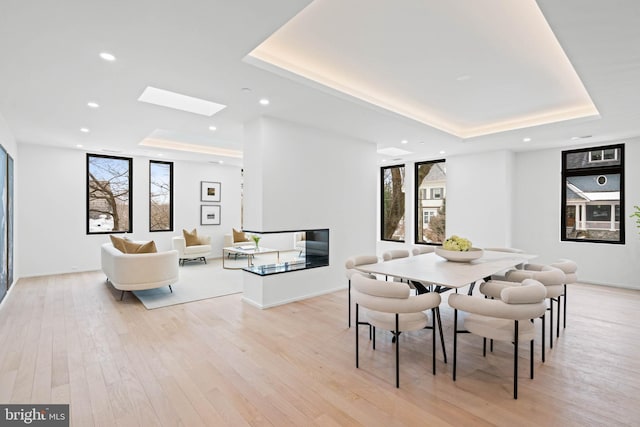 dining room featuring a tray ceiling, light hardwood / wood-style flooring, and a skylight