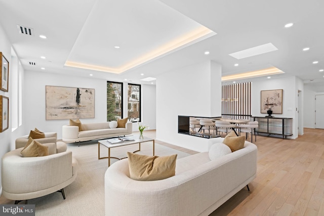 living room with a skylight, light wood-type flooring, and a raised ceiling