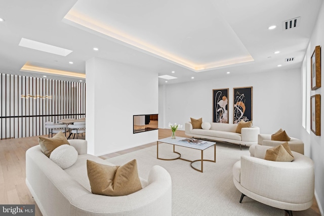 living room featuring a skylight, light hardwood / wood-style flooring, a multi sided fireplace, and a tray ceiling