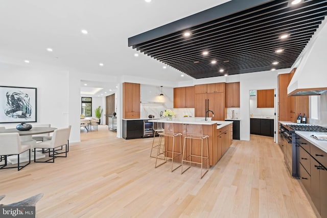 kitchen featuring a breakfast bar area, a center island with sink, light hardwood / wood-style floors, pendant lighting, and high end stainless steel range