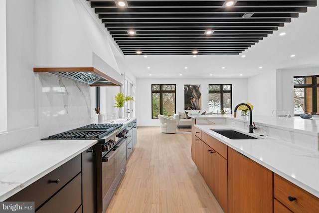 kitchen featuring light stone counters, custom range hood, gas stove, light wood-type flooring, and sink