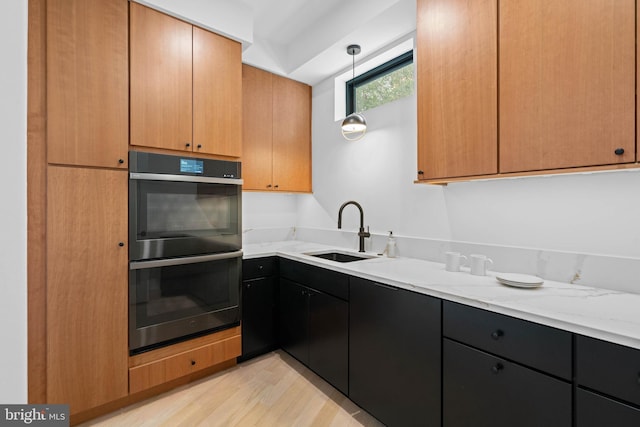 kitchen with light stone countertops, light hardwood / wood-style flooring, decorative light fixtures, double oven, and sink