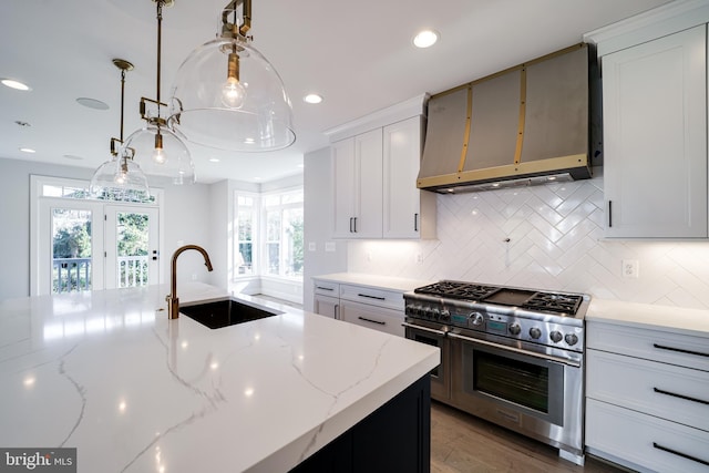 kitchen featuring range with two ovens, a sink, ventilation hood, light stone countertops, and decorative light fixtures