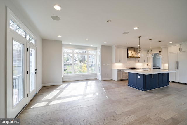 kitchen with decorative light fixtures, light countertops, white cabinetry, an island with sink, and blue cabinets