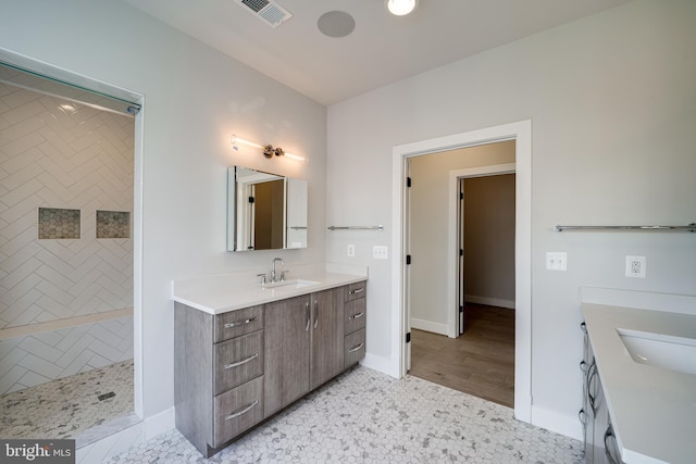 full bath featuring tiled shower, two vanities, a sink, and visible vents