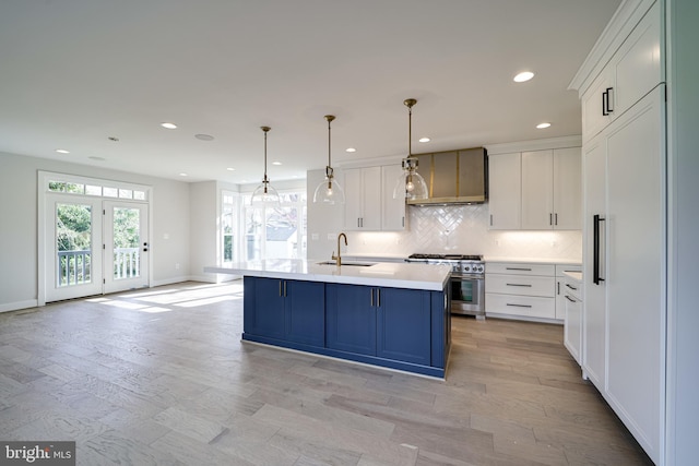 kitchen with white cabinets, light countertops, high end range, an island with sink, and pendant lighting