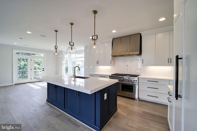 kitchen with premium appliances, decorative light fixtures, a sink, wall chimney range hood, and an island with sink