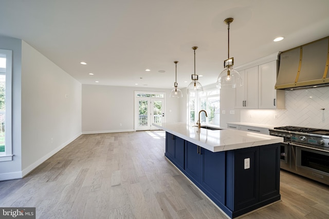 kitchen featuring decorative light fixtures, backsplash, a sink, an island with sink, and double oven range