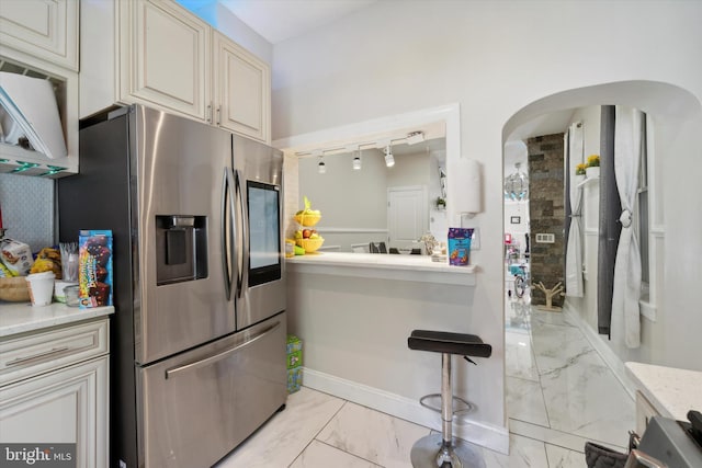 kitchen featuring light stone countertops, cream cabinets, stainless steel fridge, and rail lighting