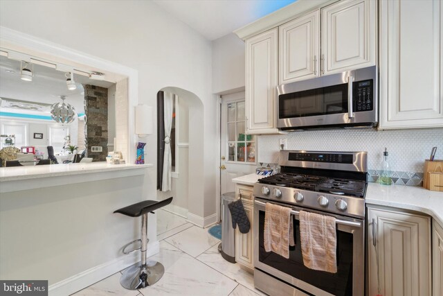 kitchen with light stone counters, rail lighting, light tile patterned floors, backsplash, and stainless steel appliances