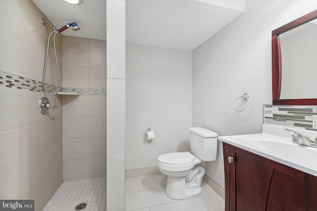 bathroom with tile patterned floors, toilet, a tile shower, vanity, and backsplash