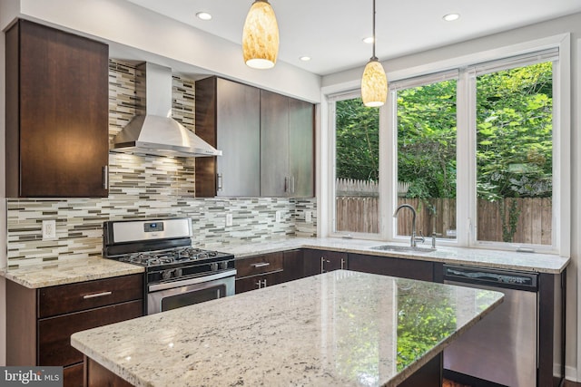 kitchen featuring sink, light stone counters, hanging light fixtures, stainless steel appliances, and wall chimney range hood