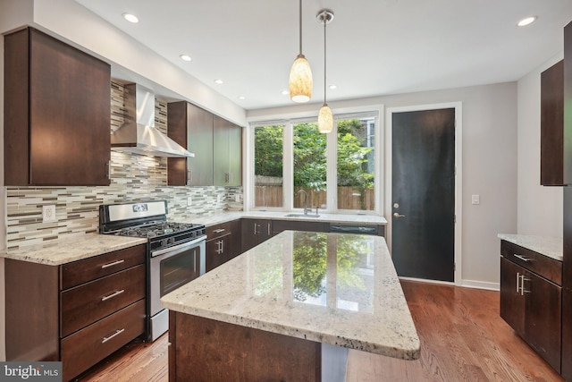 kitchen featuring wall chimney range hood, hanging light fixtures, a center island, light stone counters, and stainless steel range with gas cooktop