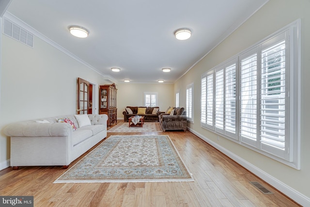 living room with a wealth of natural light, ornamental molding, and light wood-type flooring